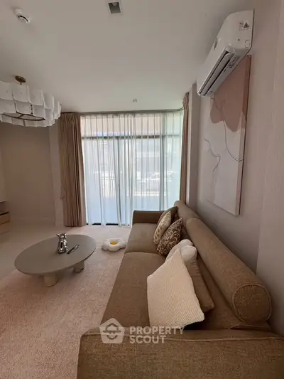 Elegant living room with modern decor, featuring a cozy sofa, stylish coffee table, and large window with sheer curtains.