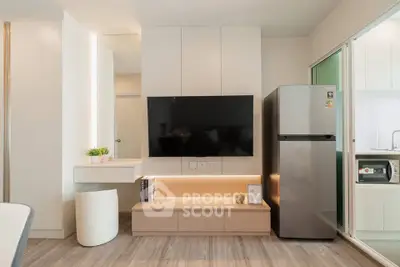 Modern living room with sleek TV setup and stainless steel fridge in stylish apartment.