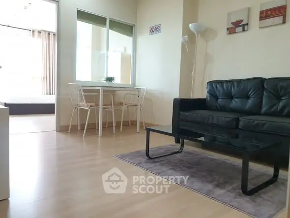 Modern living room with sleek black sofa and dining area in open layout apartment.