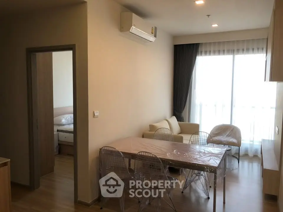 Modern apartment interior with open living and dining area, featuring a cozy sofa and large window.