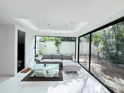 Luxurious modern living room with floor-to-ceiling windows and garden view, featuring sleek white decor and cozy seating.