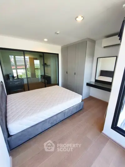 Modern bedroom with large window, built-in wardrobe, and hardwood floors in a stylish apartment.