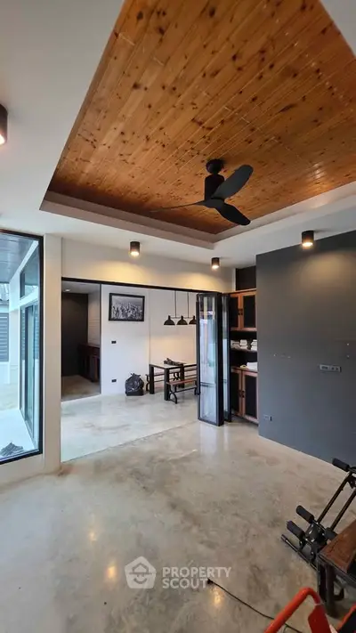 Modern living room with wooden ceiling and sleek concrete floor, featuring stylish lighting and open layout.