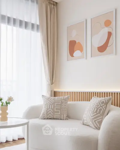 Elegant living room with modern decor and abstract art, featuring a cozy white sofa and sheer curtains.