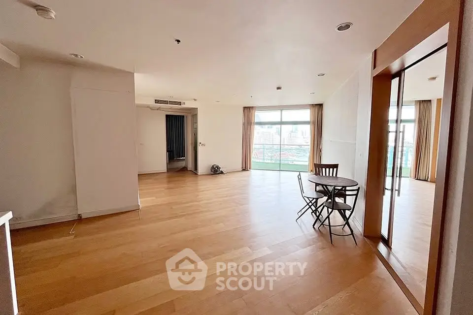 Spacious open-plan living room with wooden flooring and balcony access in modern apartment.