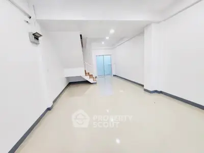 Spacious empty room with glossy tiled floor and staircase, ideal for customization.