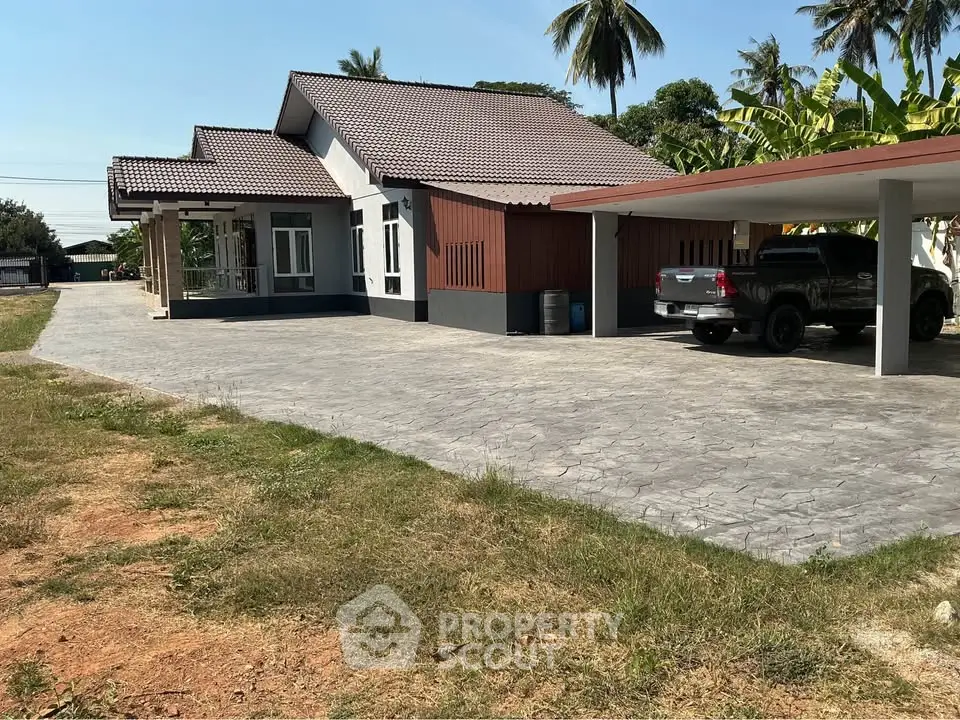 Charming single-story home with spacious driveway and carport, surrounded by lush greenery and palm trees.