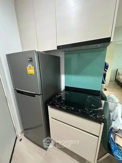 Modern kitchen with sleek cabinets and stainless steel fridge in compact layout.