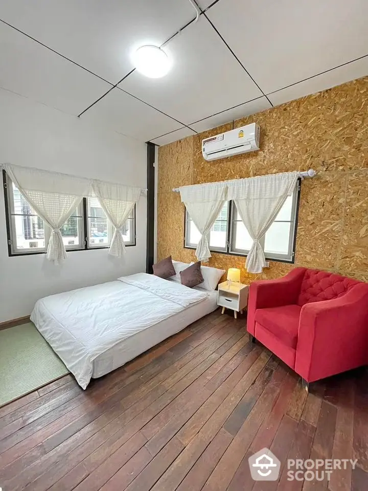 Cozy bedroom with wooden floors, red armchair, and large windows for natural light