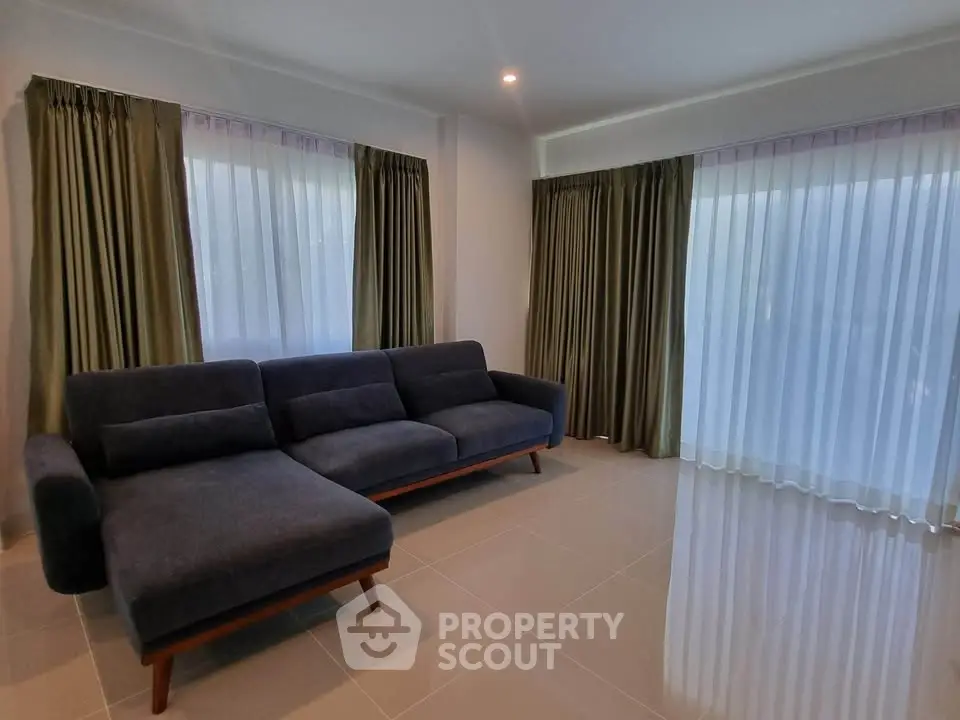 Spacious living room with modern blue sofa and large windows with curtains.