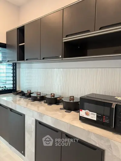 Modern kitchen with sleek cabinets and appliances, featuring a microwave and cookware on the countertop.