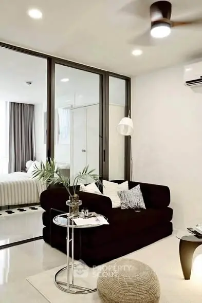 Modern living room with sleek furniture and glass partition leading to bedroom