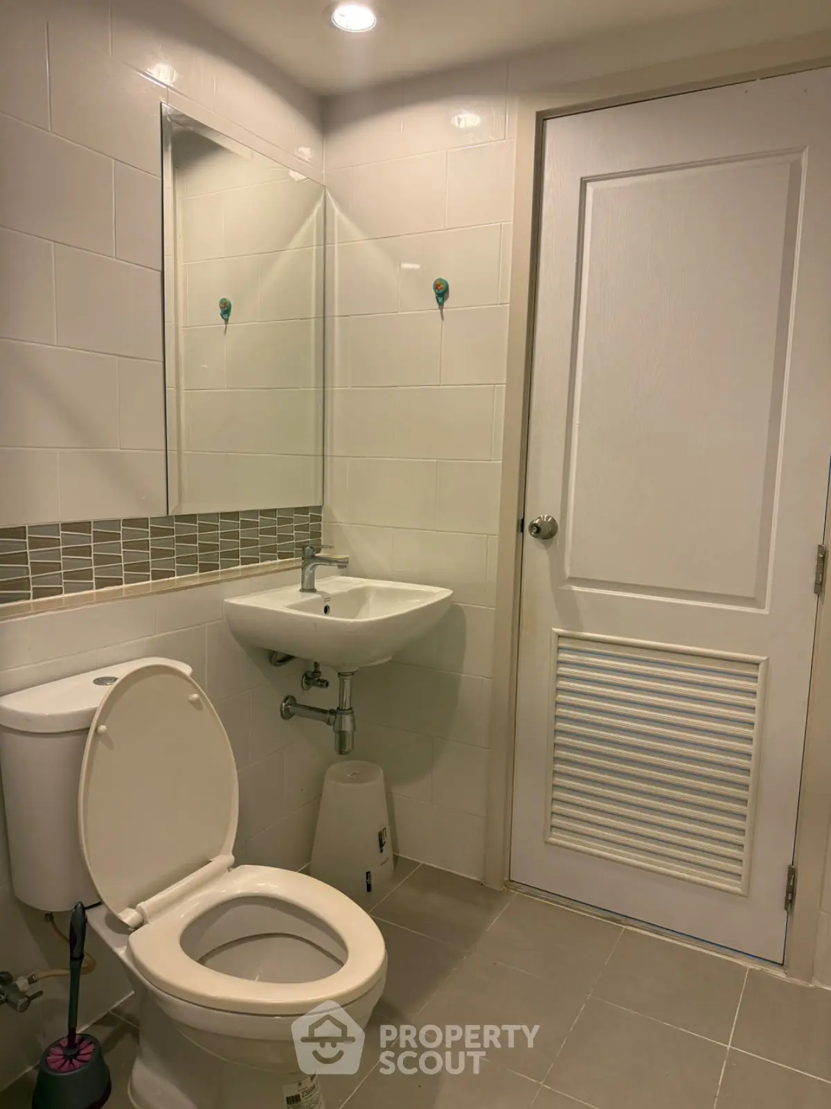 Modern bathroom with white tiles, toilet, and sink in a contemporary apartment.