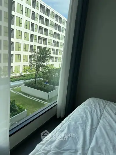 Modern apartment bedroom with large window overlooking landscaped garden and contemporary building.