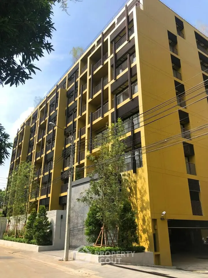 Modern yellow apartment building with lush greenery and clear blue sky.