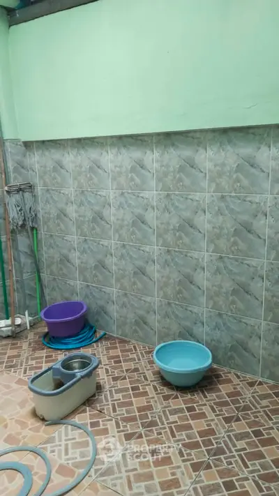 Utility area with tiled walls and cleaning supplies, ideal for laundry or storage use.