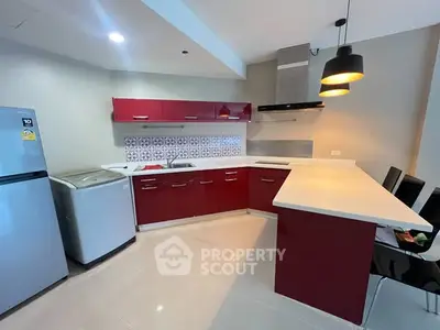 Modern kitchen with red cabinets, sleek appliances, and stylish lighting.
