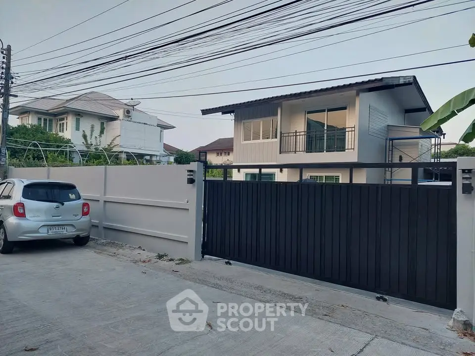 Modern two-story house with gated driveway and parked car in suburban neighborhood.