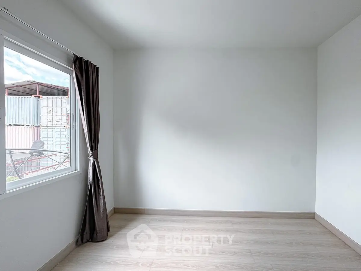 Spacious empty room with large window and wooden flooring, ready for customization.