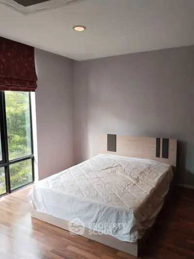 Cozy bedroom with large window and wooden flooring, perfect for natural light lovers.