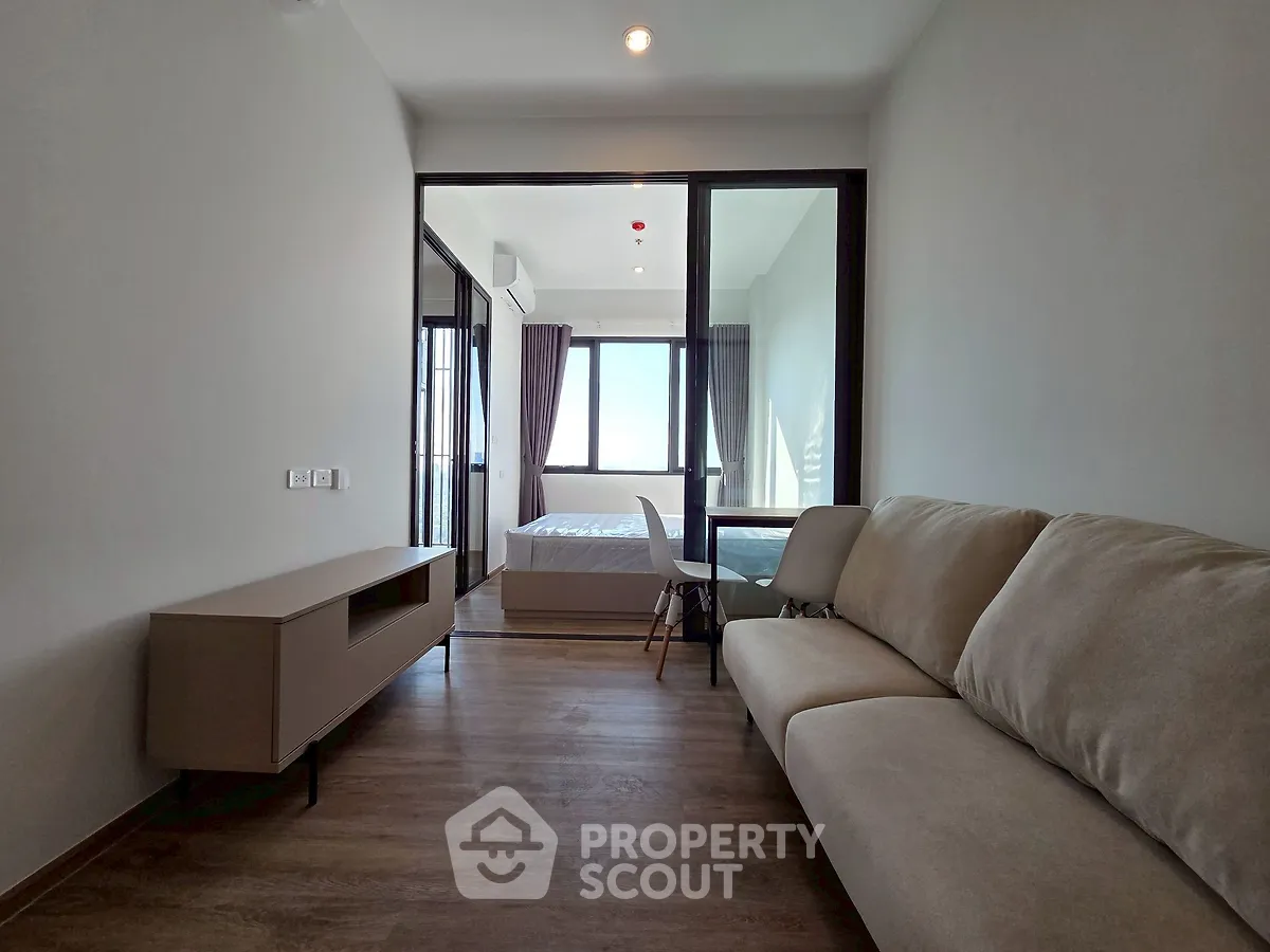 Modern living room with cozy sofa and view into bedroom, featuring sleek wooden flooring and natural light.