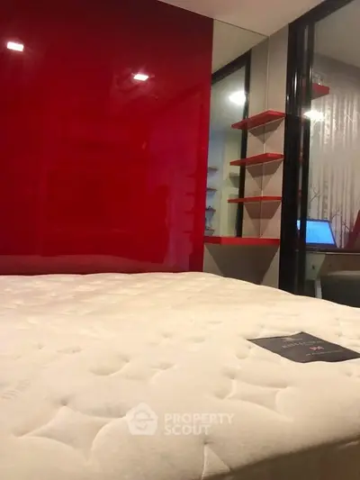 Modern bedroom with red accent wall and cozy mattress, featuring sleek shelving and a workspace.