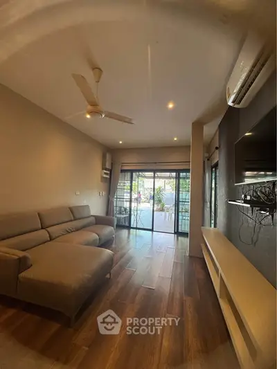 Spacious living room with modern sofa and large windows opening to a balcony, perfect for relaxation.