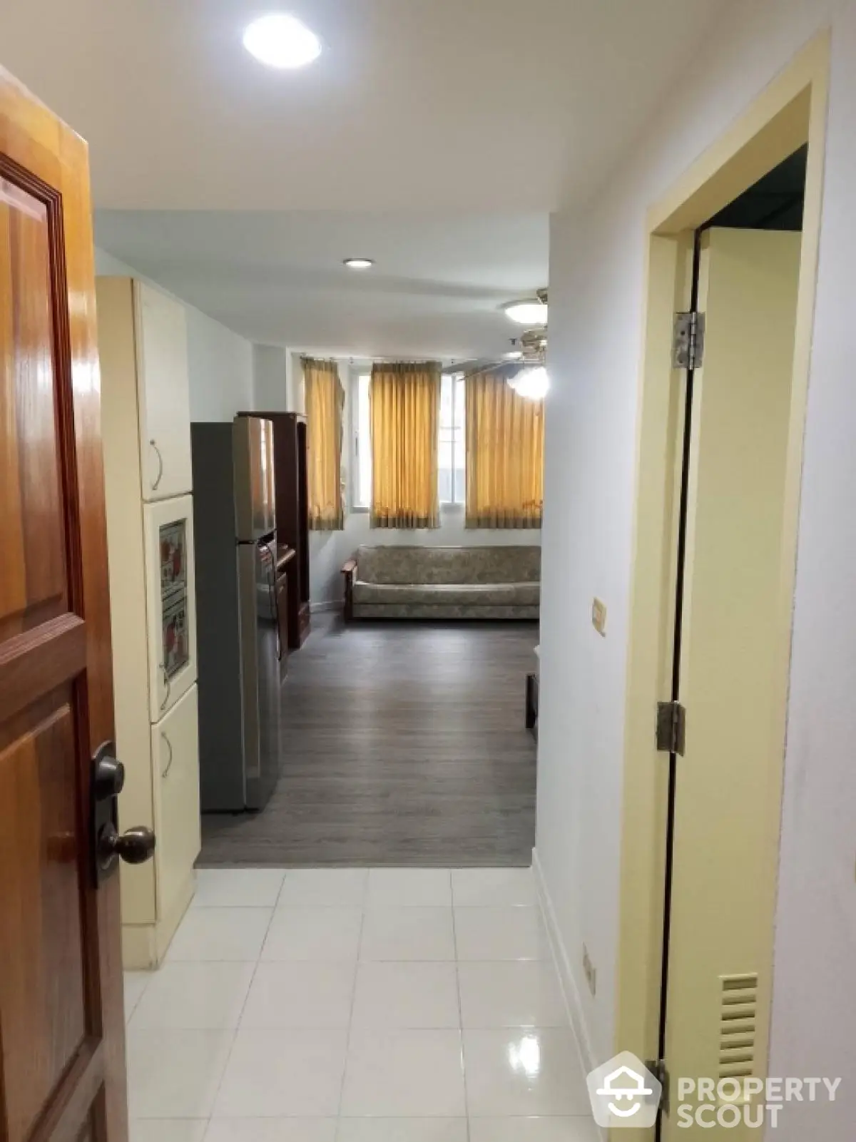 Cozy apartment entrance leading to a bright living area with wooden flooring and large windows.