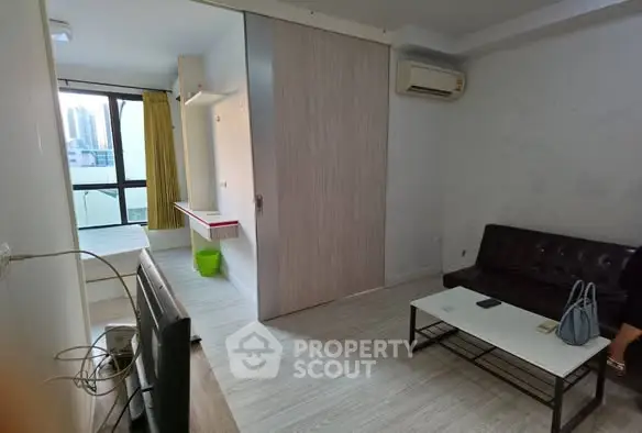 Modern living room with sleek furniture and large window offering city views.