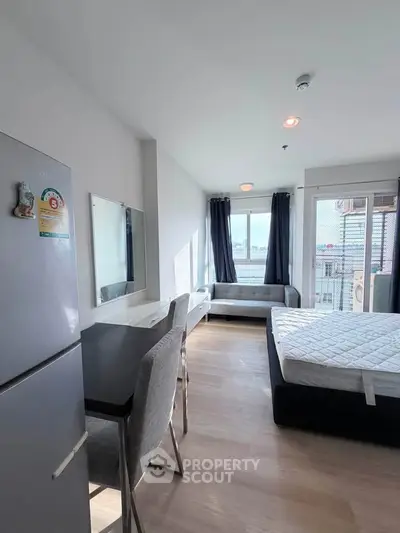 Modern studio apartment with bed, desk, and large window offering city view.