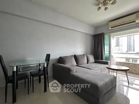 Modern living room with gray sectional sofa, glass dining table, and city view balcony.