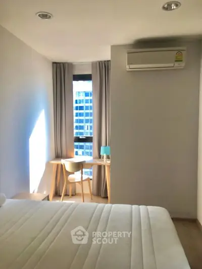 Modern bedroom with natural light, featuring a cozy workspace and air conditioning, ideal for urban living.
