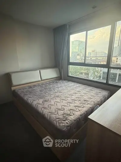 Spacious bedroom with large window offering city views, featuring a comfortable bed and modern decor.