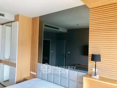 Modern bedroom with stylish wood paneling and large mirror, featuring a cozy bed and sleek lighting.