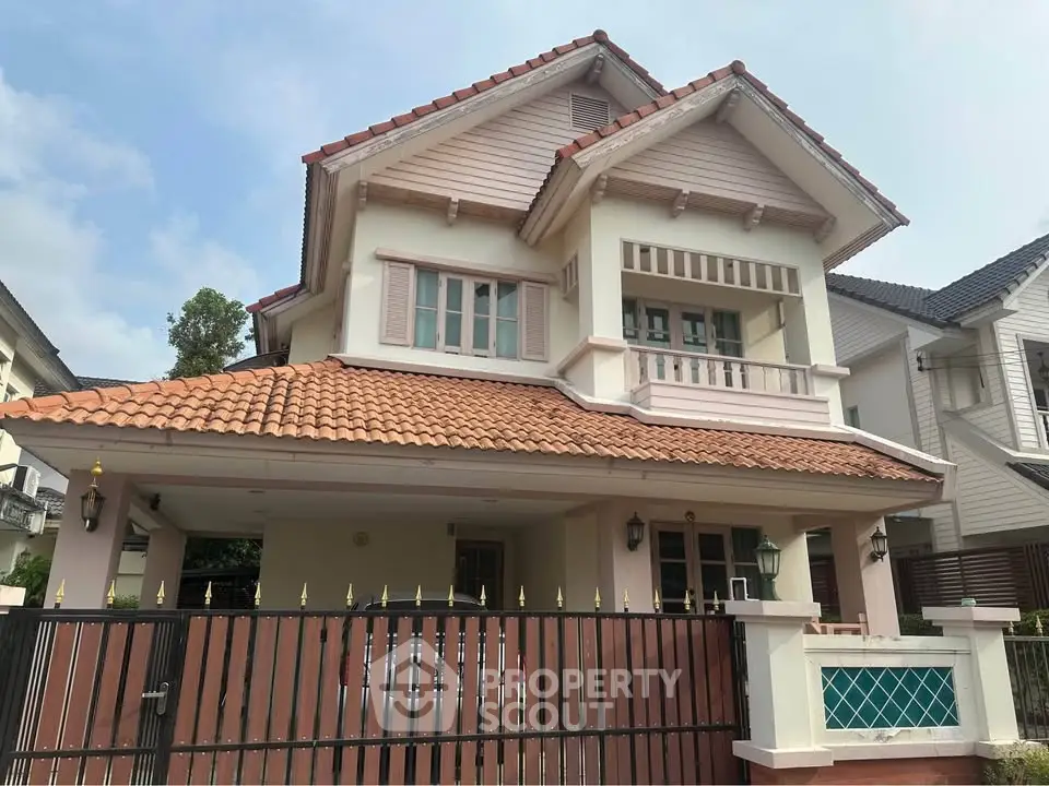 Charming two-story house with red-tiled roof and gated entrance in a suburban neighborhood.