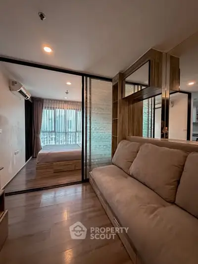 Modern apartment with cozy living room and stylish bedroom separated by glass partition.