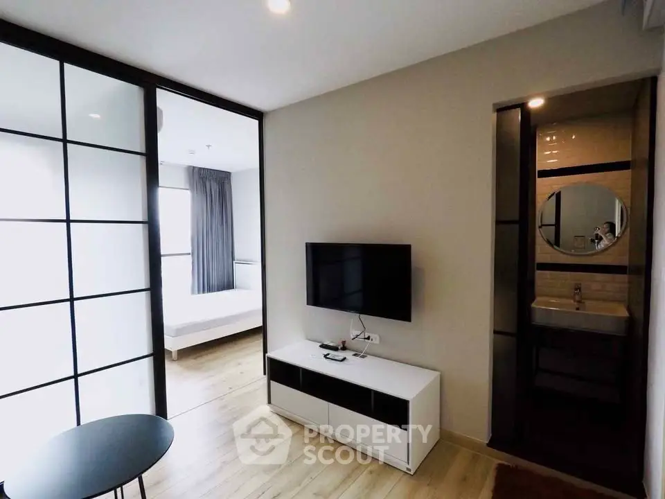Modern living room with sleek TV setup and glass partition leading to bedroom.