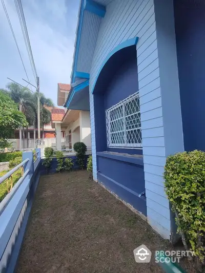 Charming blue house exterior with lush garden and secure window grilles