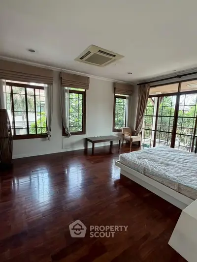 Spacious bedroom with large windows and wooden flooring, offering a serene garden view.