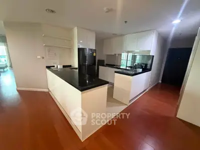 Modern kitchen with sleek black countertops and wooden flooring in a spacious apartment.