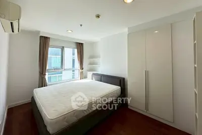 Spacious bedroom with large window and modern furnishings in a bright apartment.