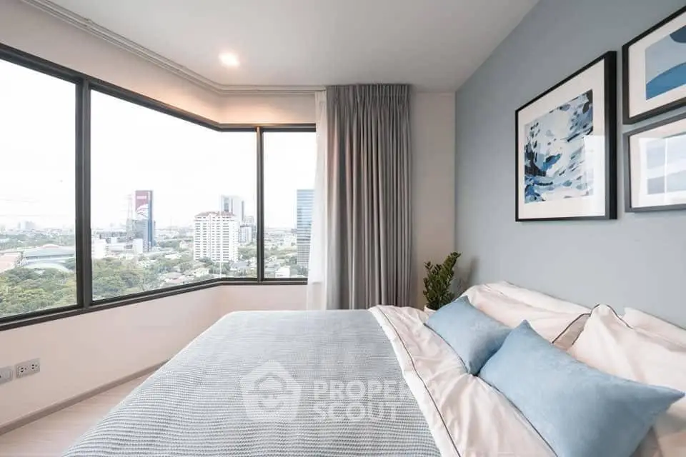 Modern bedroom with large windows offering stunning city views, elegant decor, and cozy bedding.