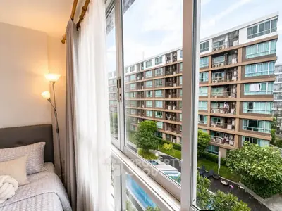 Modern bedroom with large window offering stunning view of contemporary apartment complex and lush greenery.