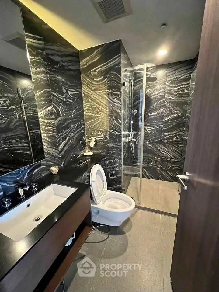 Luxurious modern bathroom with sleek black marble walls and glass shower enclosure.