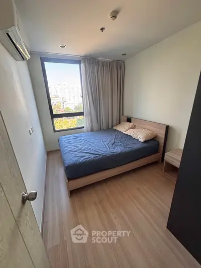 Cozy bedroom with large window and wooden flooring in modern apartment