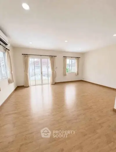 Spacious empty living room with wooden flooring and large windows for natural light.