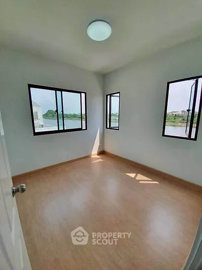Bright empty room with large windows and wooden flooring, offering a serene view, perfect for customization.
