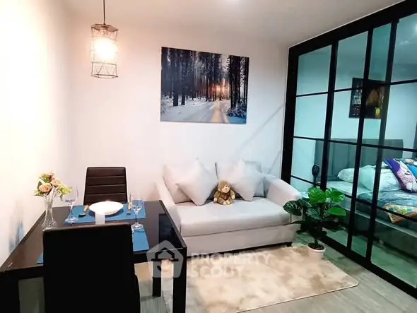 Modern living room with cozy sofa, dining table, and glass partition leading to bedroom.
