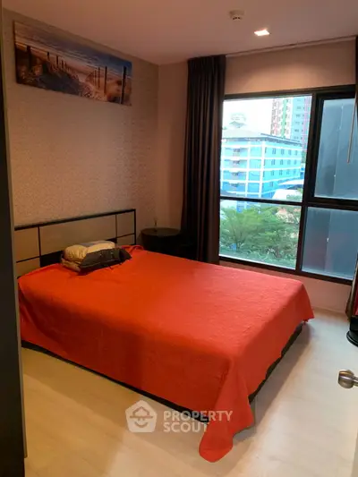 Cozy bedroom with red bedding and city view window in modern apartment.