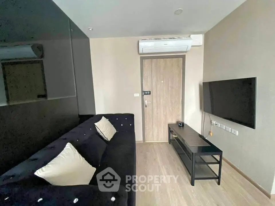 Modern living room with sleek black sofa and wall-mounted TV, featuring minimalist design and air conditioning.